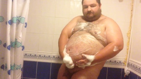 Ein Amateur-Mann mit Bauch nimmt eine seifige Dusche im Badezimmer und gibt sich dabei seinen perversen Gelüsten hin.